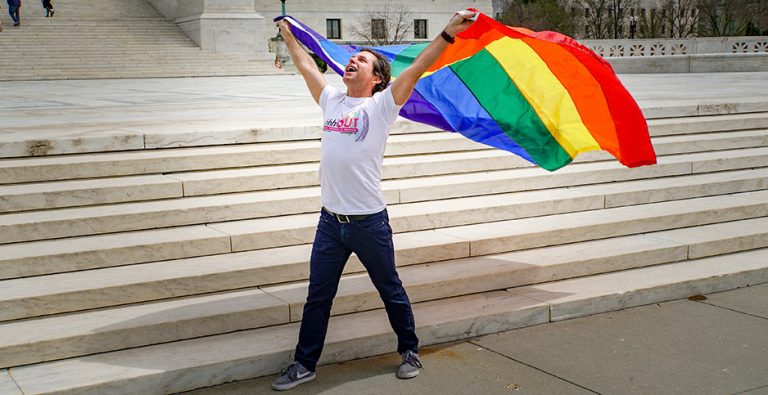 un uomo che sventola una bandiera arcobaleno simbolo della comunità LGBT+