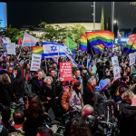 Una folla di Israeliani a una protesta contro il nuovo governo del Primo Ministro Benjamin Netanyahu, i manifestanti hanno bandiere di vario tipo (slogan in ebraico, bandiere della pace, di Israele, bandiera transgender)
