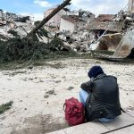 Un uomo seduto su un marciapiede di fronte ad edifici crollati per il terremoto in Turchia
