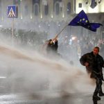 Una donna georgiana sventola una bandiera dell'Unione Europea contro gli idranti della polizia che tenta di reprimere la protesta