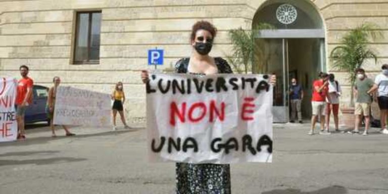 Una studentessa dell'Università del Salento mostra uno striscione con sopra scritto: "L'Università non è una gara"