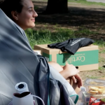 una studentessa dentro a una tenda in un parco, di fronte alla tenda si vedono un thermos e del civo