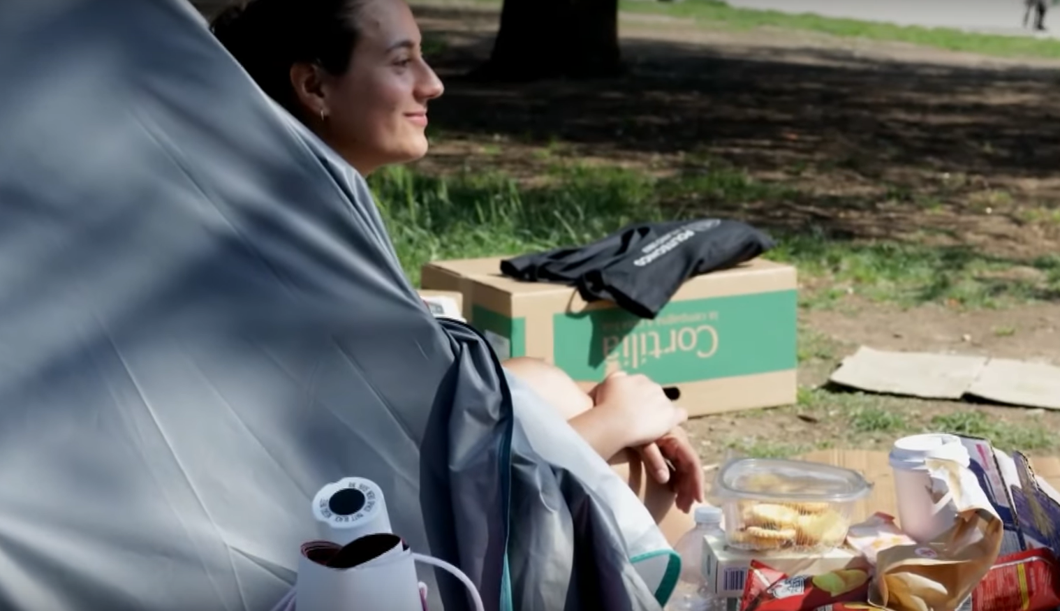 una studentessa dentro a una tenda in un parco, di fronte alla tenda si vedono un thermos e del civo