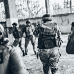 Tre militari avanzano in una struttura chiusa, seguiti da due persone in mimetica e con antiproiettili con la scritta "PRESS"