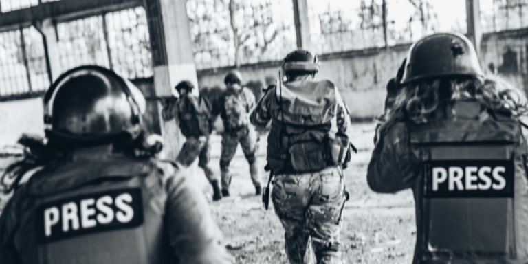 Tre militari avanzano in una struttura chiusa, seguiti da due persone in mimetica e con antiproiettili con la scritta "PRESS"
