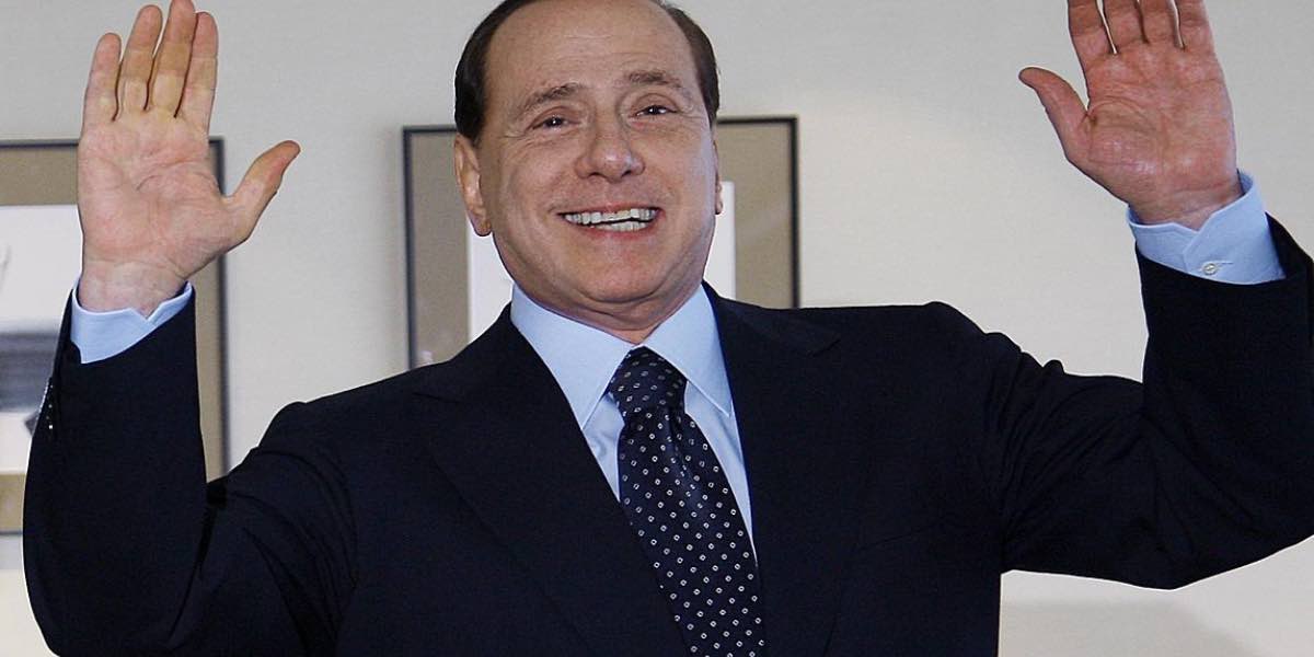 Silvio Berlusconi sorridente con le mani alzate.