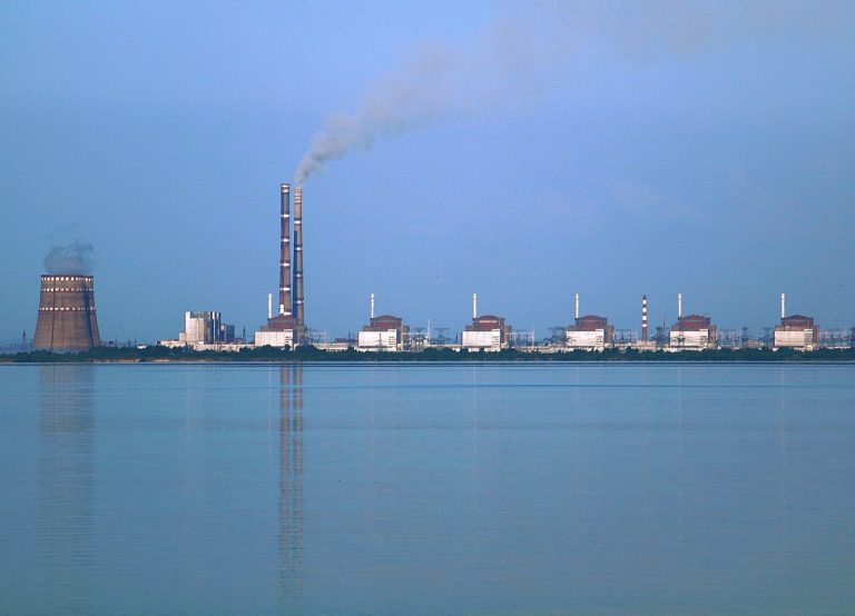 Due centrali elettriche a Enerhodar, a circa 50 km da Zaporižžja in Ucraina, viste dall'altra parte del bacino di Kakhovka sul fiume Dnieper. Foto scattata dalla riva di "Nikopol". La centrale più vicina è la Zaporizhzhia Nuclear Power Plant, la più grande centrale nucleare d'Europa, composta da due torri di raffreddamento (una in gran parte oscurata dall'altra) sulla sinistra e da 6 edifici per reattori VVER. Il grande edificio tra le torri di raffreddamento e i reattori e le due alte ciminiere si trovano nella centrale termica di Zaporizhzhia, a circa 3 km dalla centrale nucleare.