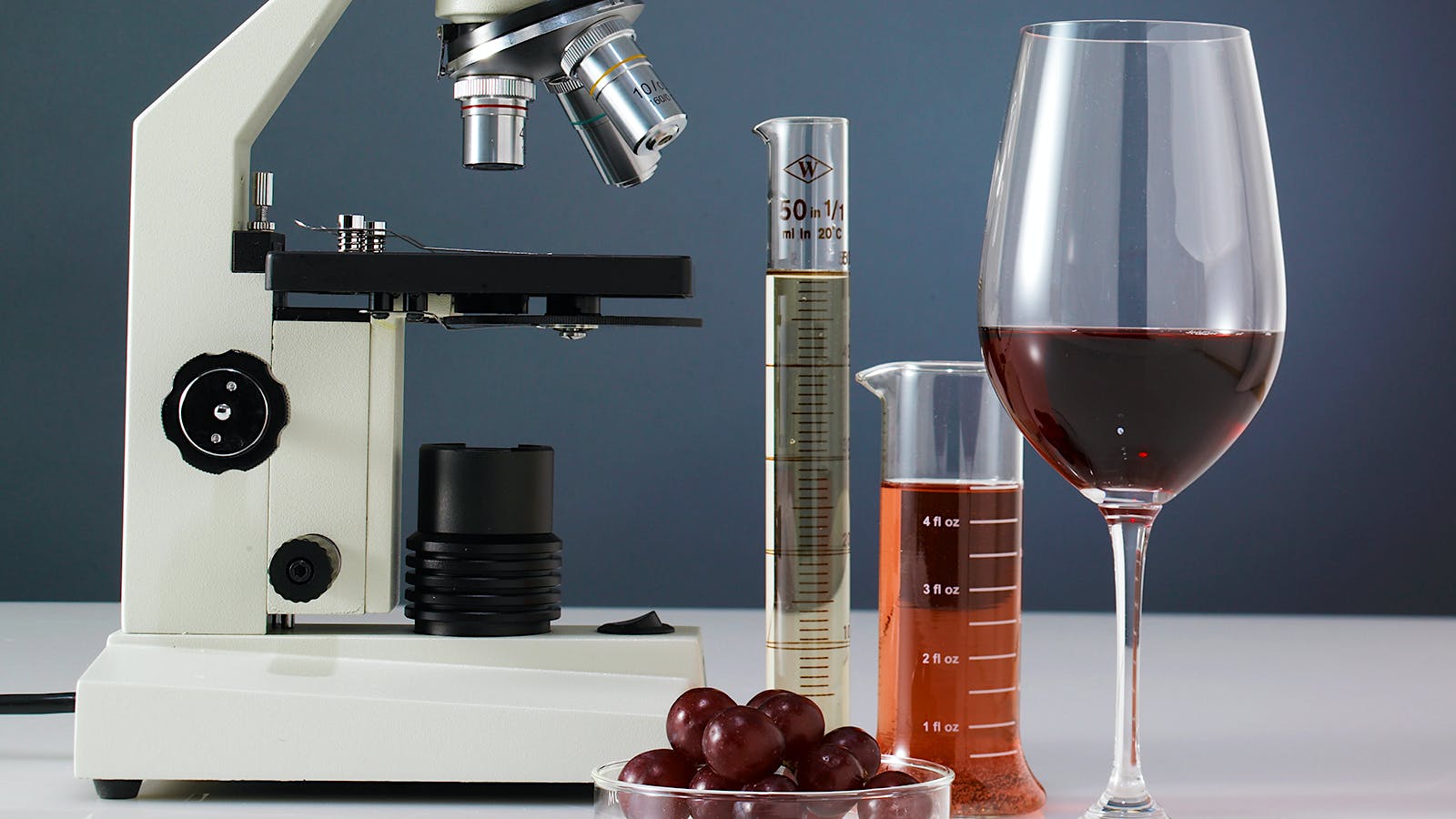 Un bicchiere di vino rosso, delle provette e un microscopio per fare delle analisi sui rapporti tra vino e cancro. Cosa dicono gli studi scientifici?