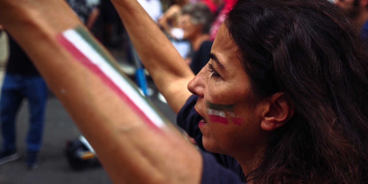 Una donna con la bandiera dell'Iran dipinta sulle guance manifesta a Roma a un anno dalla morte di Jina Mahsa Amini. Nonostante le proteste siano meno frequenti e abbiano perso l'intensità dell'inizio, l’anniversario della morte di Jina Mahsa Amini è stato celebrato con iniziative e manifestazioni di solidarietà in diverse città in tutto il mondo. Abbiamo raccolto le voci della diaspora iraniana in Italia.