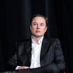 Elon Musk seduto su uno poltrona con alle spalle uno sfondo nero