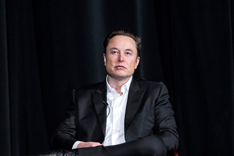 Elon Musk seduto su uno poltrona con alle spalle uno sfondo nero