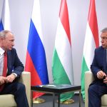 Vladimir Putin, a sinistra, seduto su una poltroncina guarda Vitkor Orbán. In mezzo ai due un tavolino. Sullo sfondo, quattro bandiere (due russe e due ungheresi, da sinistra verso destra)