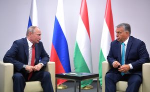 Vladimir Putin, a sinistra, seduto su una poltroncina guarda Vitkor Orbán. In mezzo ai due un tavolino. Sullo sfondo, quattro bandiere (due russe e due ungheresi, da sinistra verso destra)