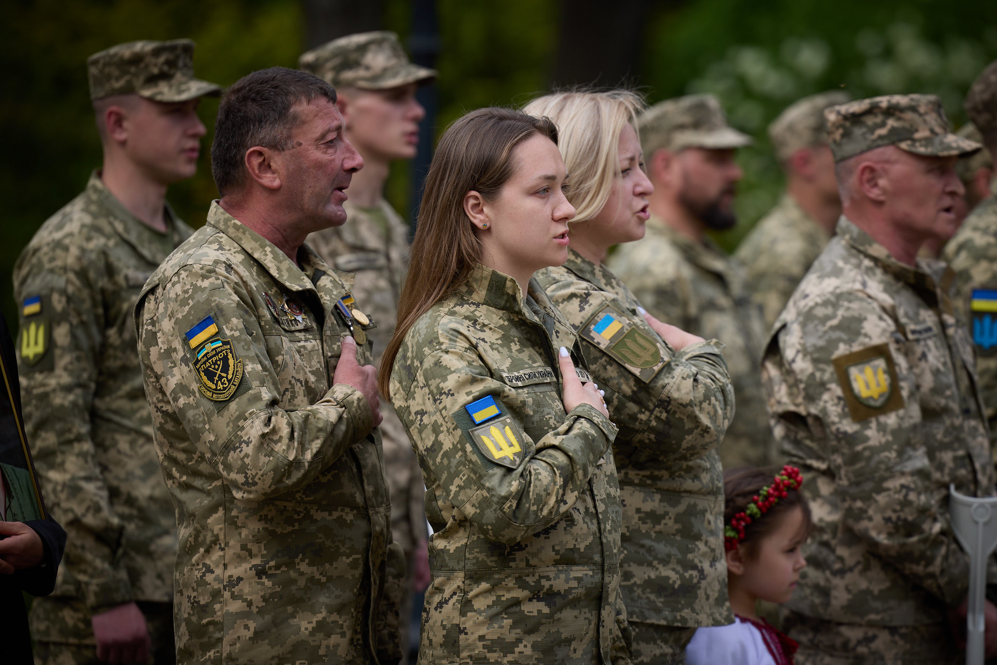 soldati ucraini alllineati, da sinistra a destra tre uomini, due donne e tre uomini (tutti di profilo destro). L'uomo al centro e le due donne hanno la mano sul petto.