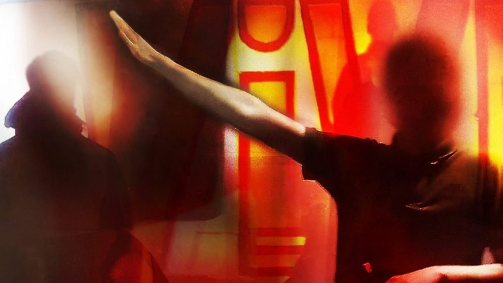 Una persona dal volto oscurato si esibisce in un saluto romano. L'inchiesta di Fanpage sulla gioventù meloniana, l'ala giovanile di Fratelli d'Italia solleva molte domande: le risposte non stanno arrivando, tra silenzi e caos informativo.