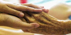 Una mano di una caregiver tiene nelle sue le mani di una persona anziana. In Italia non c'è ancora una legge nazionale sul fine vita