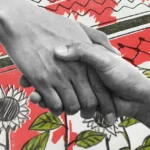 Due mani si stringono. Sullo sfondo una bandiera rossa con fiori e piante