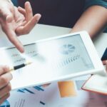 Delle mani di alcuni collaboratori su laptop e carta. Come cambieranno il lavoro aziendale le AI?