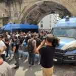due camionette della polizia con davanti un gruppo di agenti, circondate da giornalisti e manifestanti.