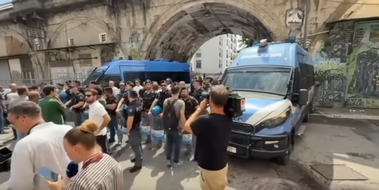 due camionette della polizia con davanti un gruppo di agenti, circondate da giornalisti e manifestanti.