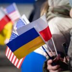 Un rifugiato ucraino ha in mano le bandierine dell'Ucraina, della Polonia e degli Stati Uniti