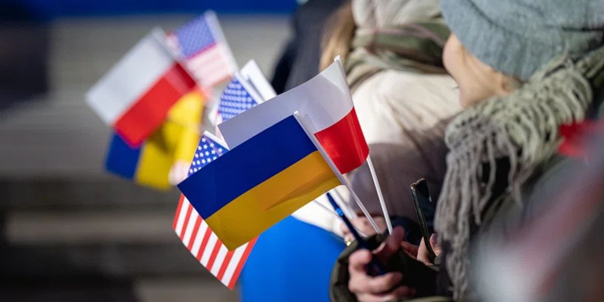 Un rifugiato ucraino ha in mano le bandierine dell'Ucraina, della Polonia e degli Stati Uniti