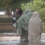 Due uomini vanno in soccorso di due donne di spalle nelle strade in Pakistan inondate dall'alluvione
