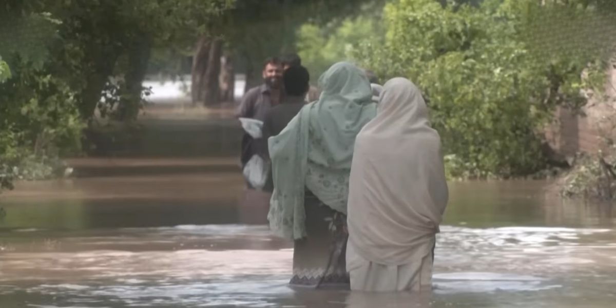 Due uomini vanno in soccorso di due donne di spalle nelle strade in Pakistan inondate dall'alluvione