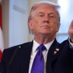 Trump punta l'indice. Sullo sfondo la bandiera degli Stati Uniti